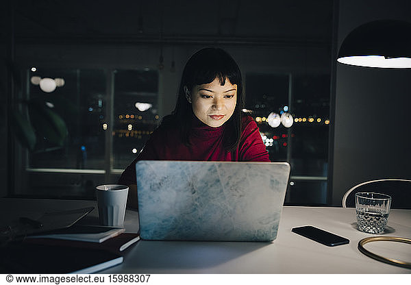 Confident young female professional using laptop while working late in creative workplace