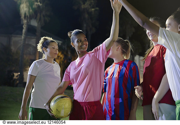 Confident young female soccer teammates high-fiving on field at night