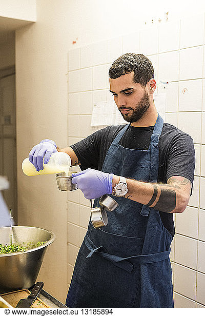 Confident young male chef pouring ingredient in container at restaurant commercial kitchen