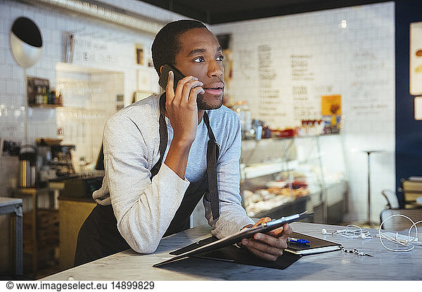 Confident young male employee talking through smart phone while leaning at delicatessen