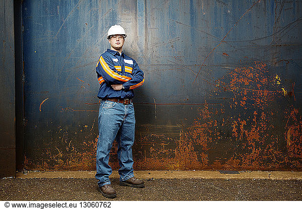 Confident young male worker with arms crossed standing against metal wall