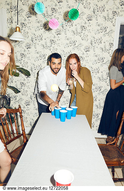 Confident young man playing beer pong on table by female friend at dinner party