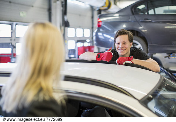 Confident young mechanic showing thumbs up to female customer over car