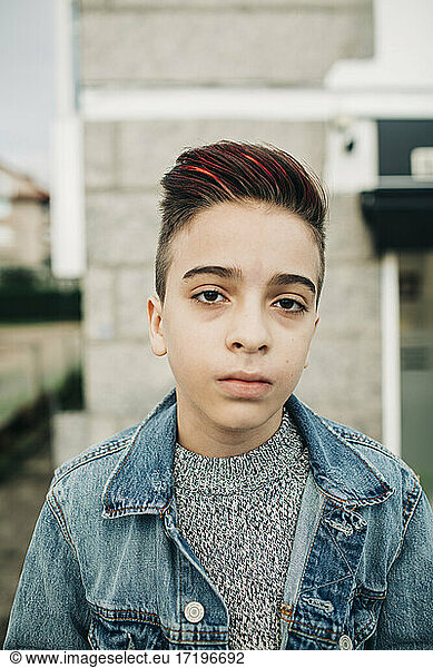 Confident young teen boy with red highlights hair and denim by wall