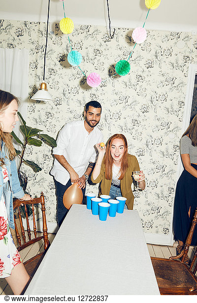 Confident young woman playing beer pong on table by male friend at dinner party