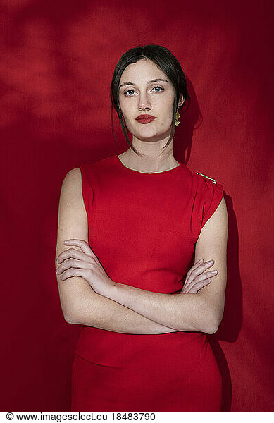 Confident young woman standing with arms crossed against red background
