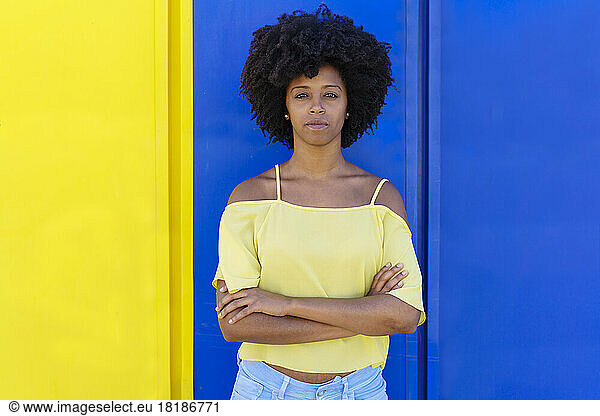 Confident young woman standing with arms crossed in front of two tone color wall