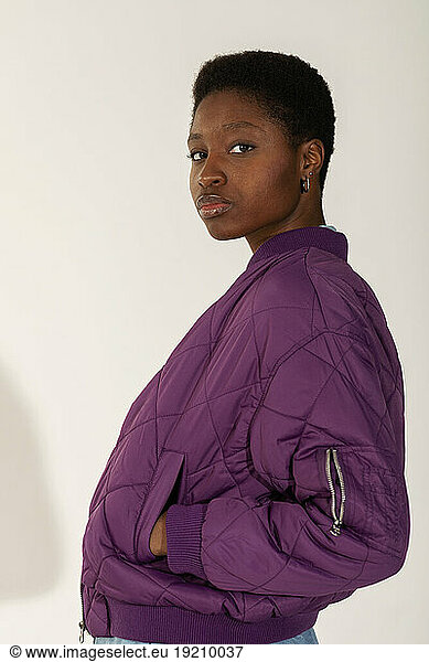 Confident young woman standing with hands in pockets against white background