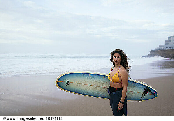 Confident young woman with surfboard at beach on vacation