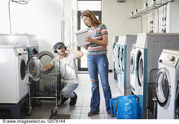 Confused university student showing detergent pack to male friend at laundromat