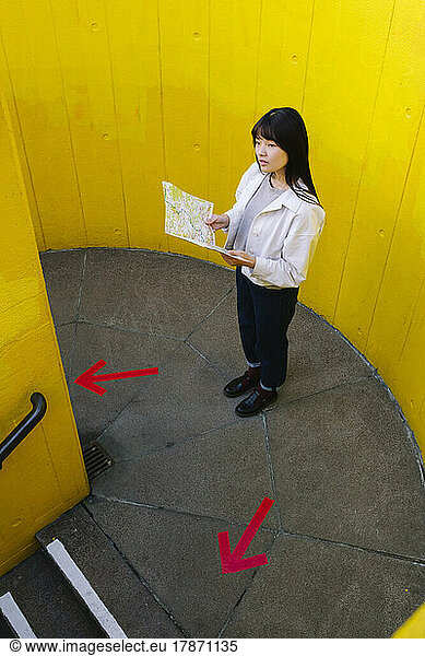 Confused woman holding map standing in front of wall
