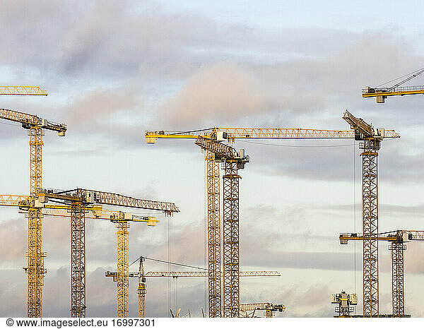 Construction cranes standing against sky at dusk