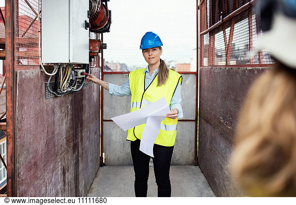 Construction manager holding documents while showing machinery in construction elevator
