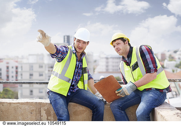 Construction worker and engineer with clipboard pointing at highrise construction site