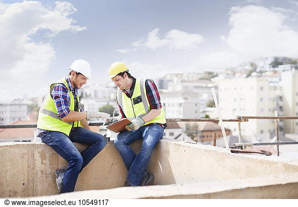 Construction worker and engineer with clipboard talking at highrise construction site