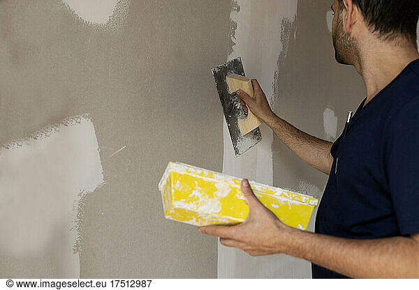 Construction worker plastering wall in a house