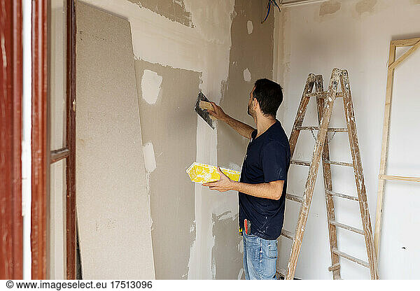 Construction worker plastering wall in a house