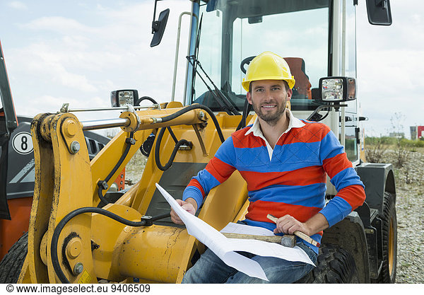 Construction worker sitting on excavator holding construction plan