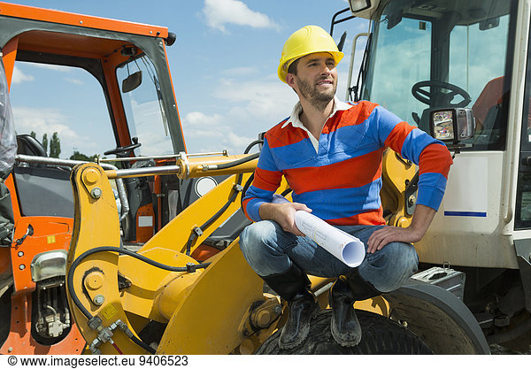 Construction worker sitting on excavator holding construction plan