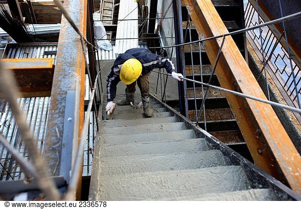 Construction worker smoothing concrete with masons float on stairs