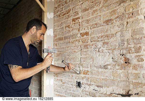 Construction worker using hammer and chisel at a brick wall
