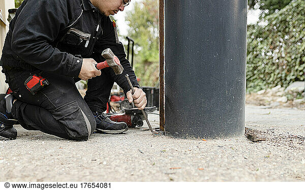 Construction worker with hammer working by metal pillar