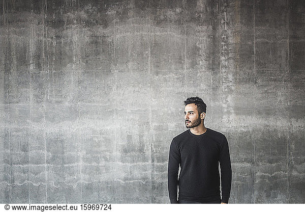 Contemplating man looking away while standing against gray wall