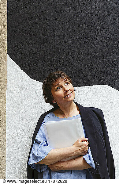 Contemplating woman holding folder in front of wall