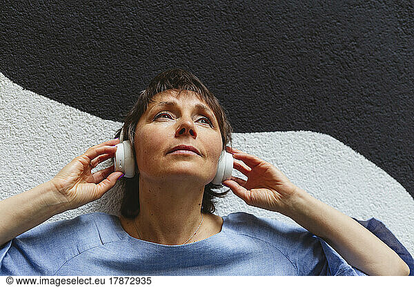 Contemplating woman listening music in front of wall