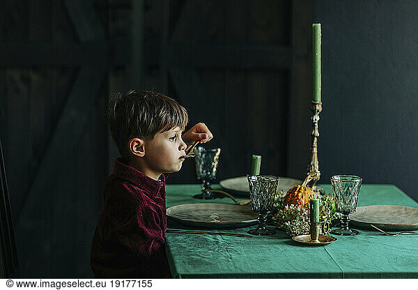 Contemplative boy eating from spoon at dining table