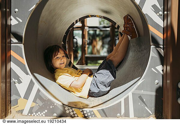 Contemplative boy lying inside outdoor play equipment