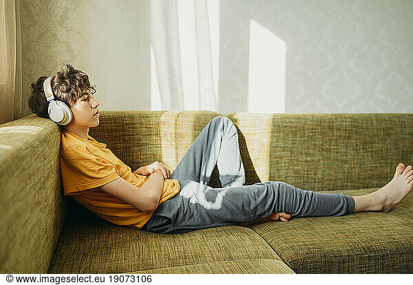 Contemplative boy wearing headphones relaxing on sofa