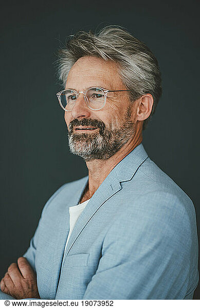 Contemplative businessman wearing eyeglasses against teal background