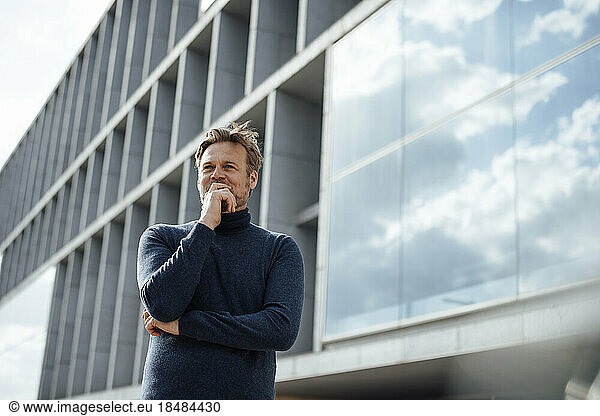 Contemplative businessman with hand on chin in front of modern office building