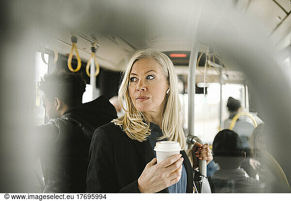 Contemplative businesswoman holding disposable cup while commuting through bus