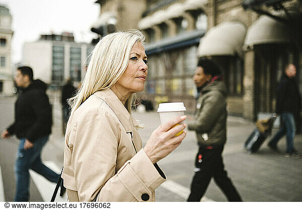 Contemplative businesswoman holding disposable cup while crossing street in city