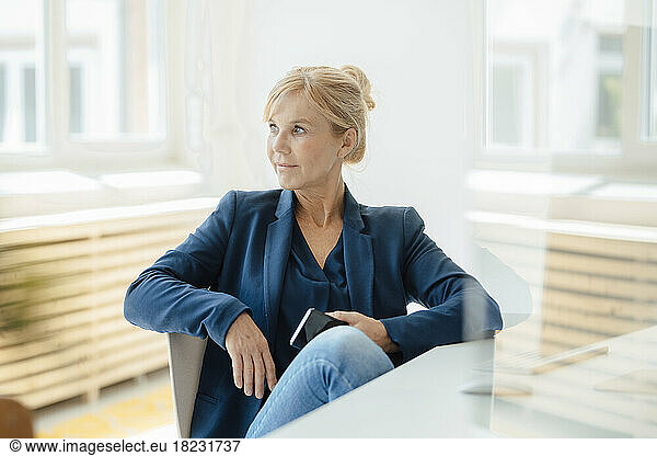Contemplative businesswoman with mobile phone seen through glass