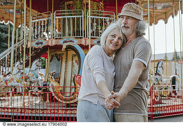 Contemplative couple standing together in front of carousel