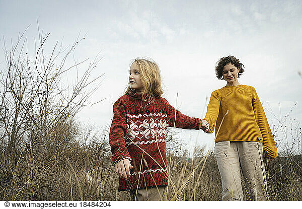 Contemplative daughter holding hands with mother under sky