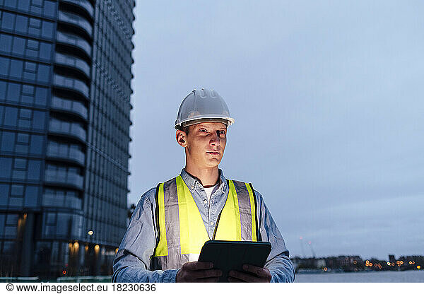 Contemplative engineer with tablet PC wearing reflective clothing