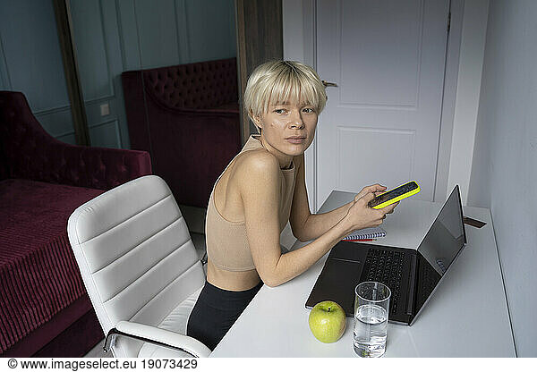 Contemplative freelancer holding smart phone near desk at home