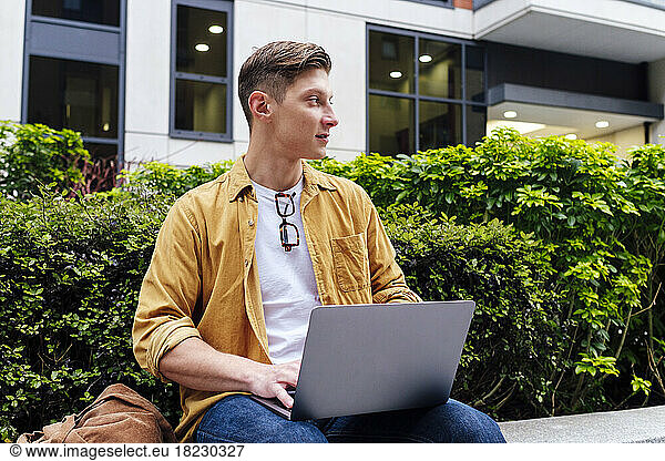 Contemplative freelancer with laptop sitting near plants