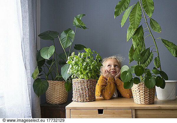 Contemplative girl by houseplants on table at home