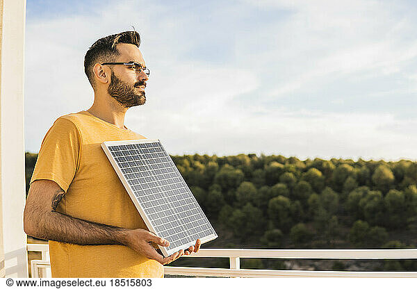 Contemplative man holding solar panel on terrace
