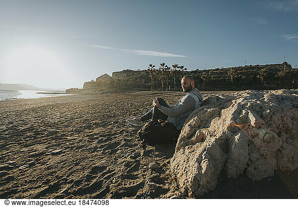 Contemplative man sitting by rock at beach