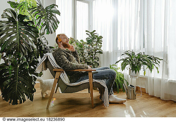 Contemplative man wearing headphones sitting on chair at home