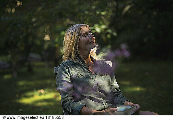 Contemplative mature woman sitting with book in garden