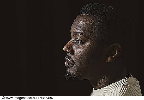 Contemplative mid adult man by black background in studio