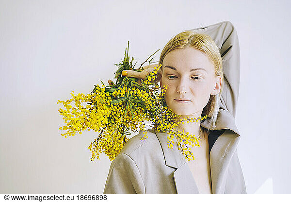 Contemplative woman holding bunch of mimosa flowers against white background