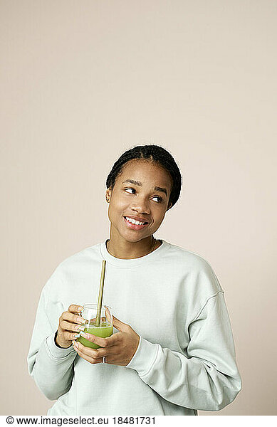 Contemplative woman holding green smoothie in front of wall